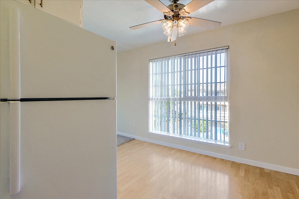 an empty living room with a large window and a refrigerator