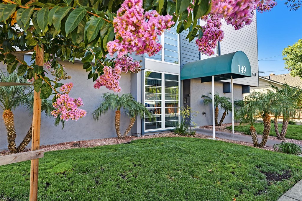 the front of a building with green grass and pink flowers