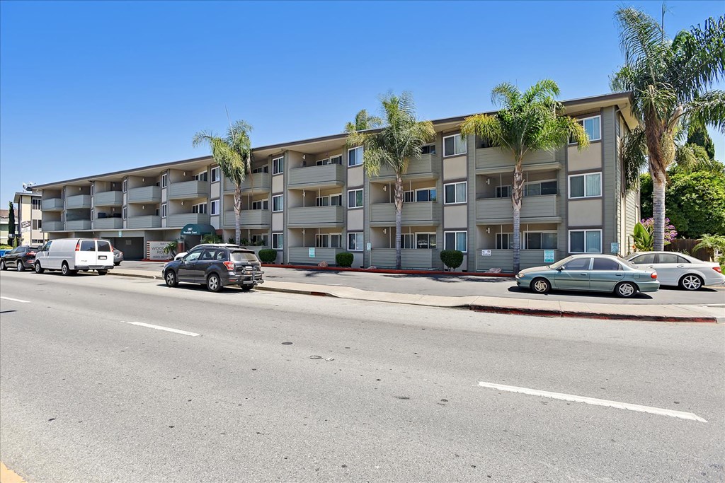 A street view of a residential building with cars parked in front.