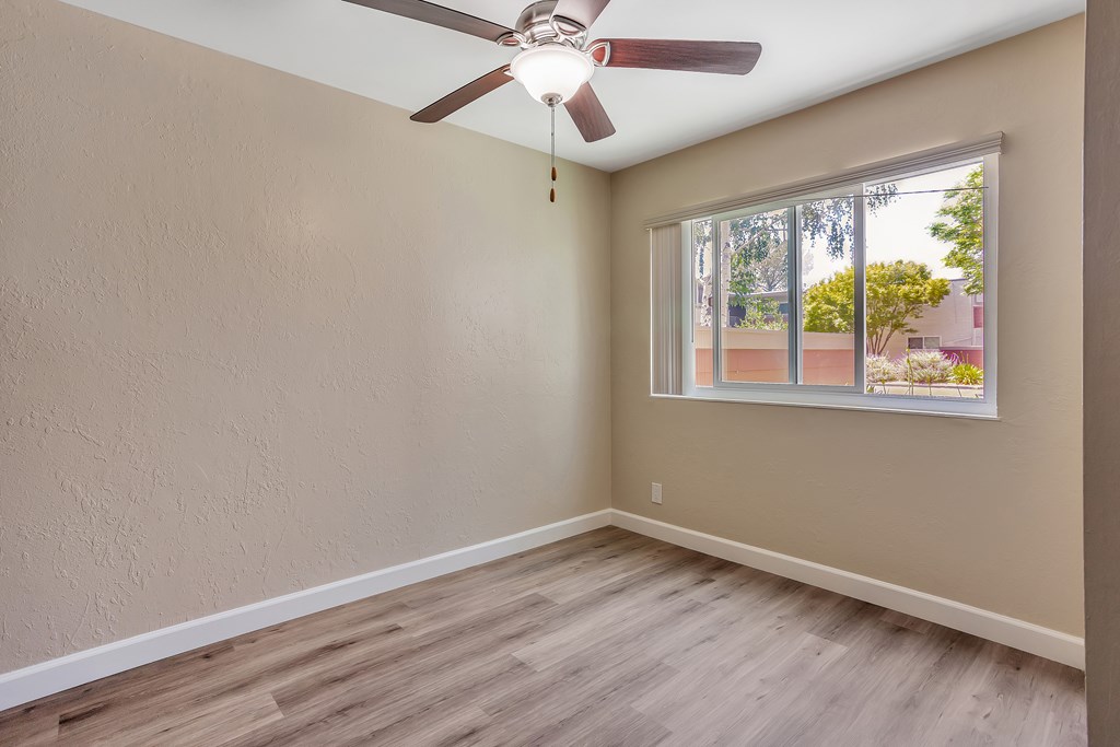 A room with a ceiling fan and a window overlooking a building.