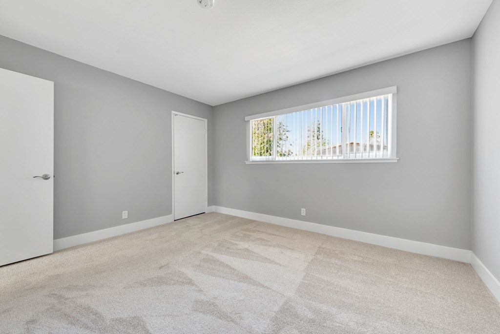 A room with a carpeted floor and a window with blinds.
