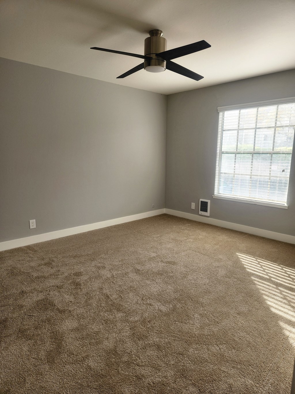 an empty carpeted room with a ceiling fan and a window