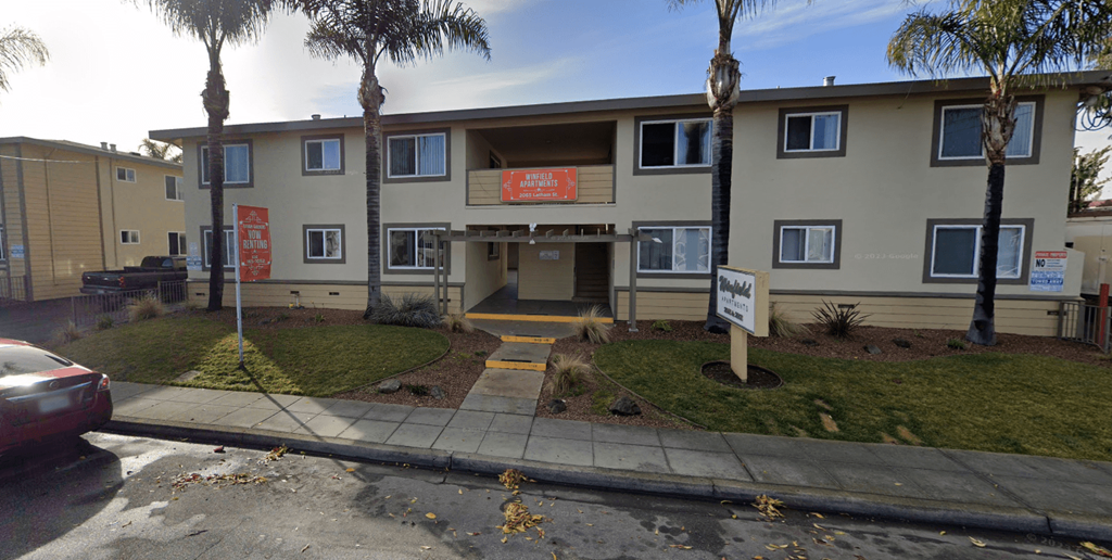 the front of an apartment building with palm trees