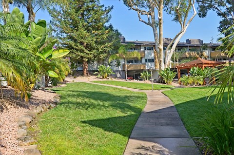 A walkway leads through a grassy area with trees and apartment buildings in the background.