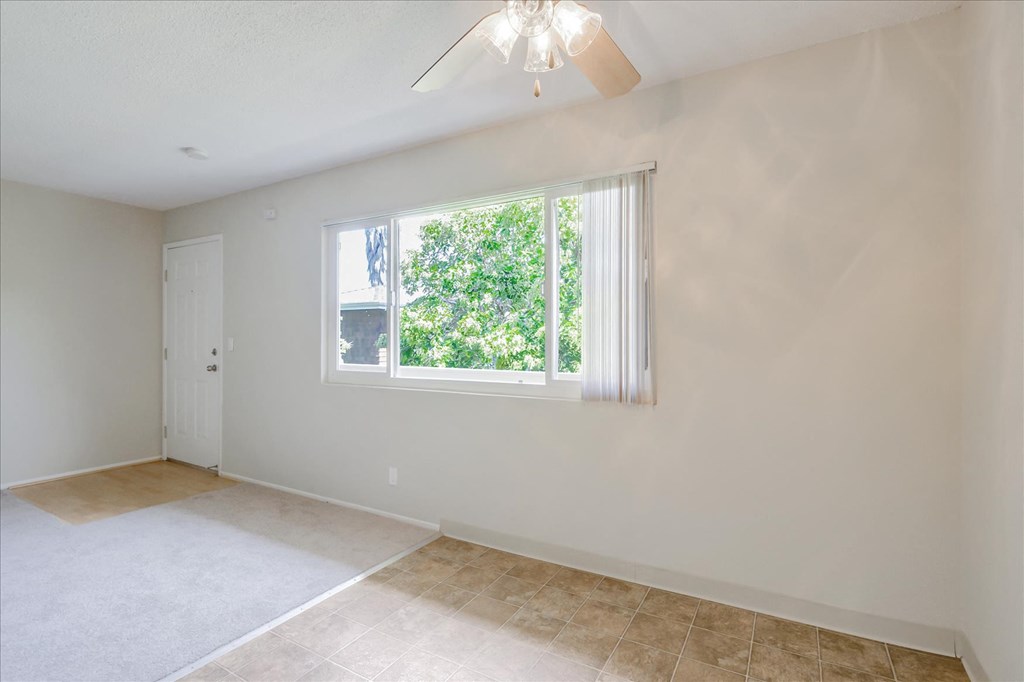an empty living room with a window and a ceiling fan