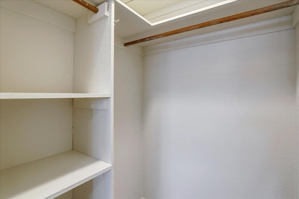 a walk in closet with white shelves and a window