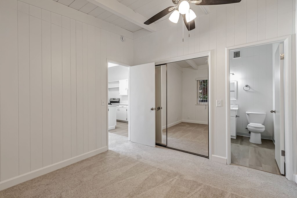 A room with a ceiling fan and a sliding glass door leading to a bathroom.