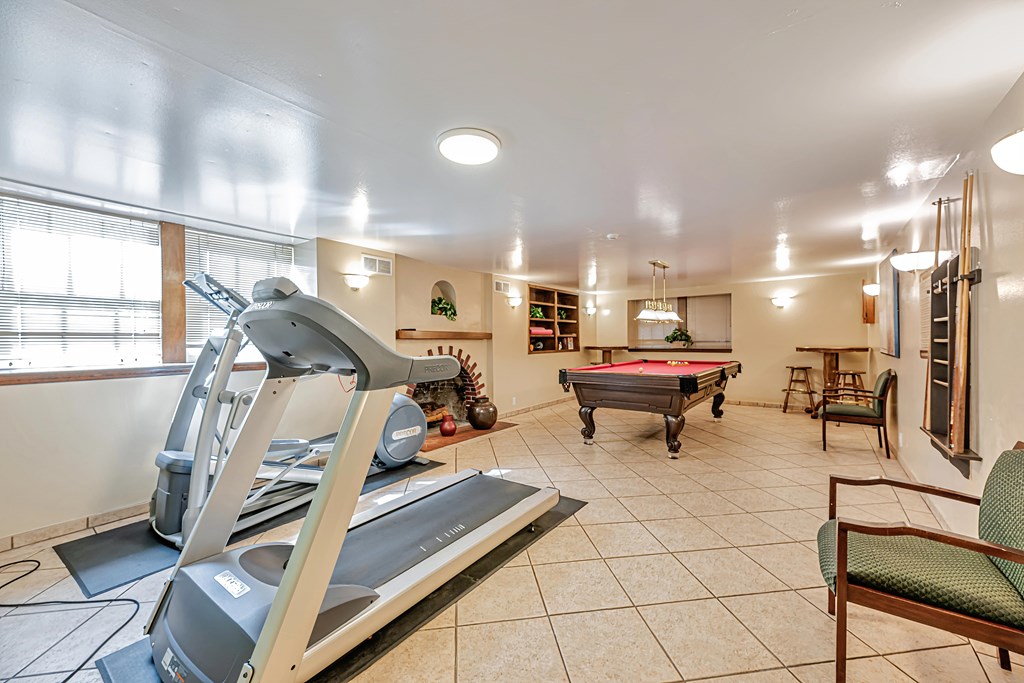 A treadmill is in the middle of a room with a pool table and a chair.