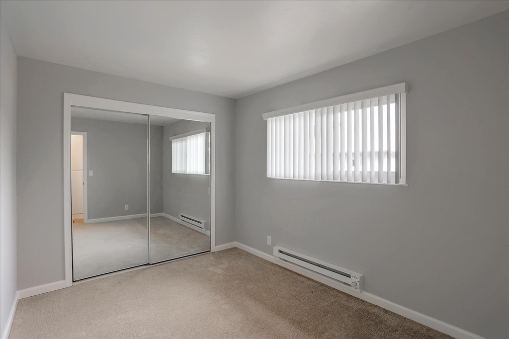 A room with a carpeted floor, a window with blinds, and a sliding glass door.