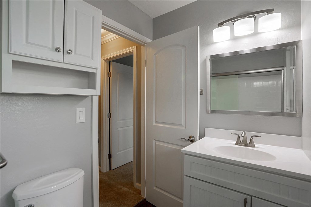 A white bathroom with a toilet, sink, and mirror.