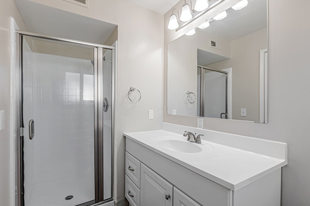 A white bathroom with a sink, mirror, and shower.