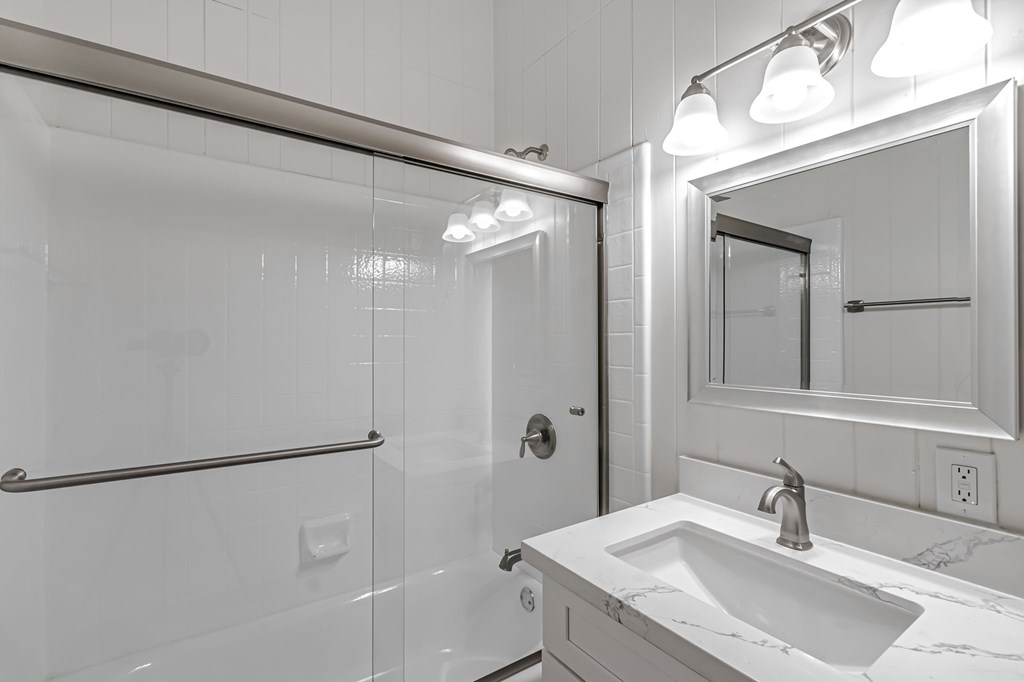 A white bathroom with a sink, mirror, and shower.