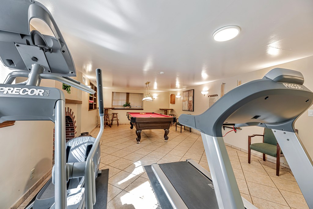 A treadmill is in the foreground of a well-lit room with a ping pong table and a green chair.