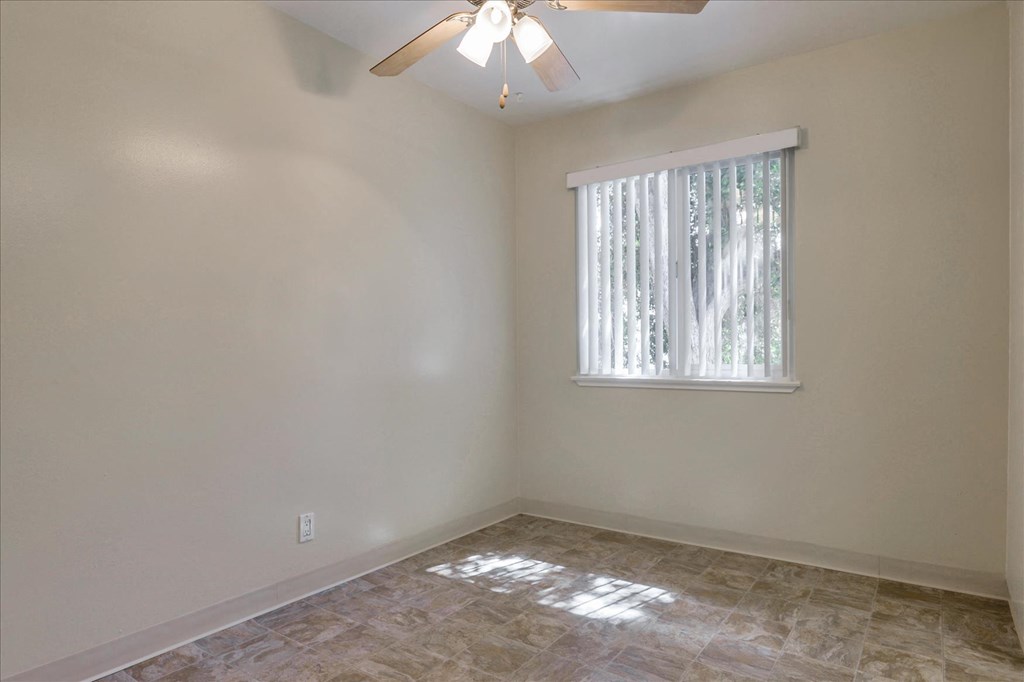 A room with a ceiling fan and a window with blinds.