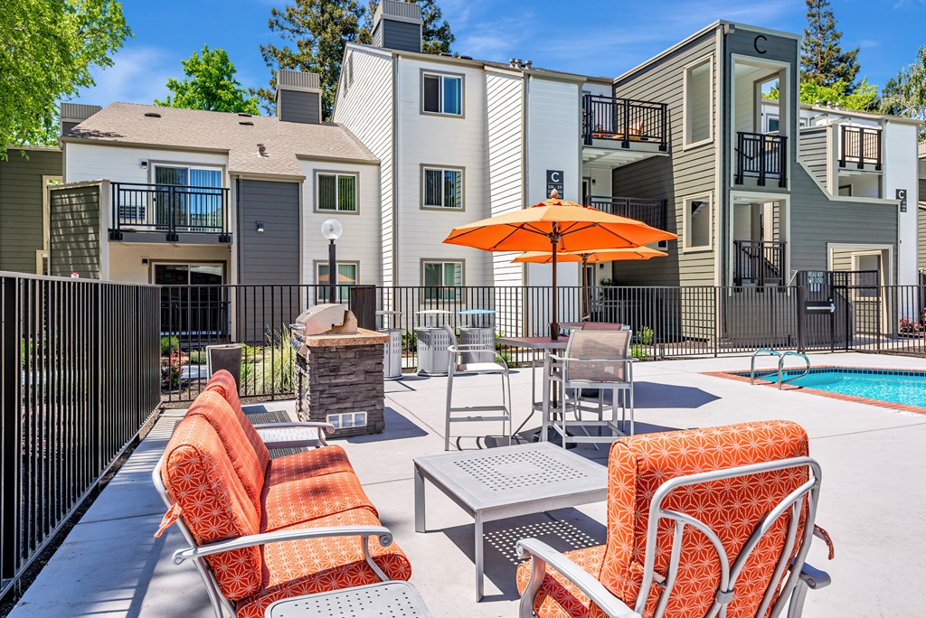 A patio with chairs and an umbrella in front of apartment buildings.