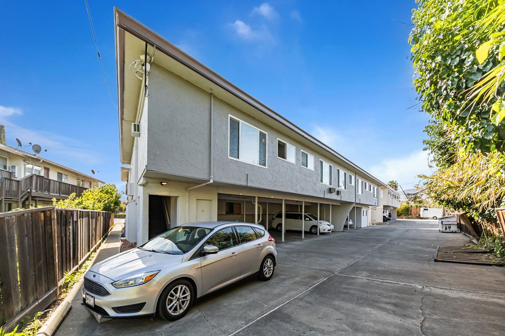 A silver car is parked in a driveway in front of a two-story building.