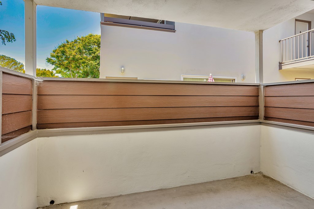 A balcony with a white wall and brown wooden slats.