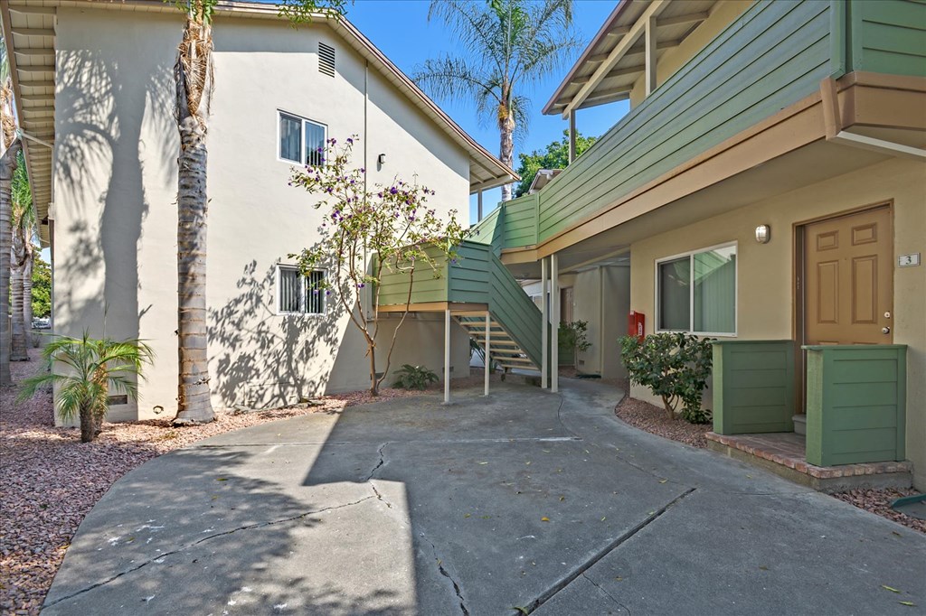 a driveway in front of a white house with a wooden door