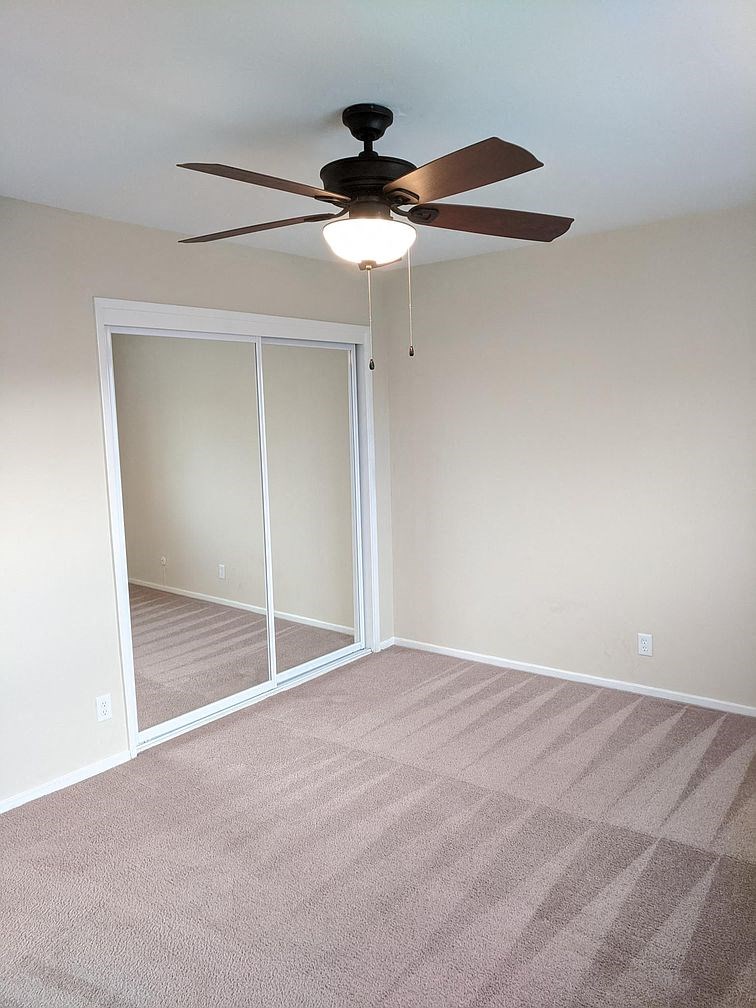 an empty room with a ceiling fan and a mirrored closet