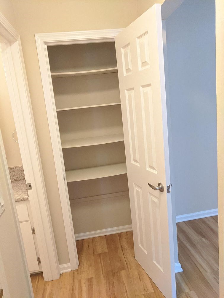 A white pantry with a door open to a hallway.