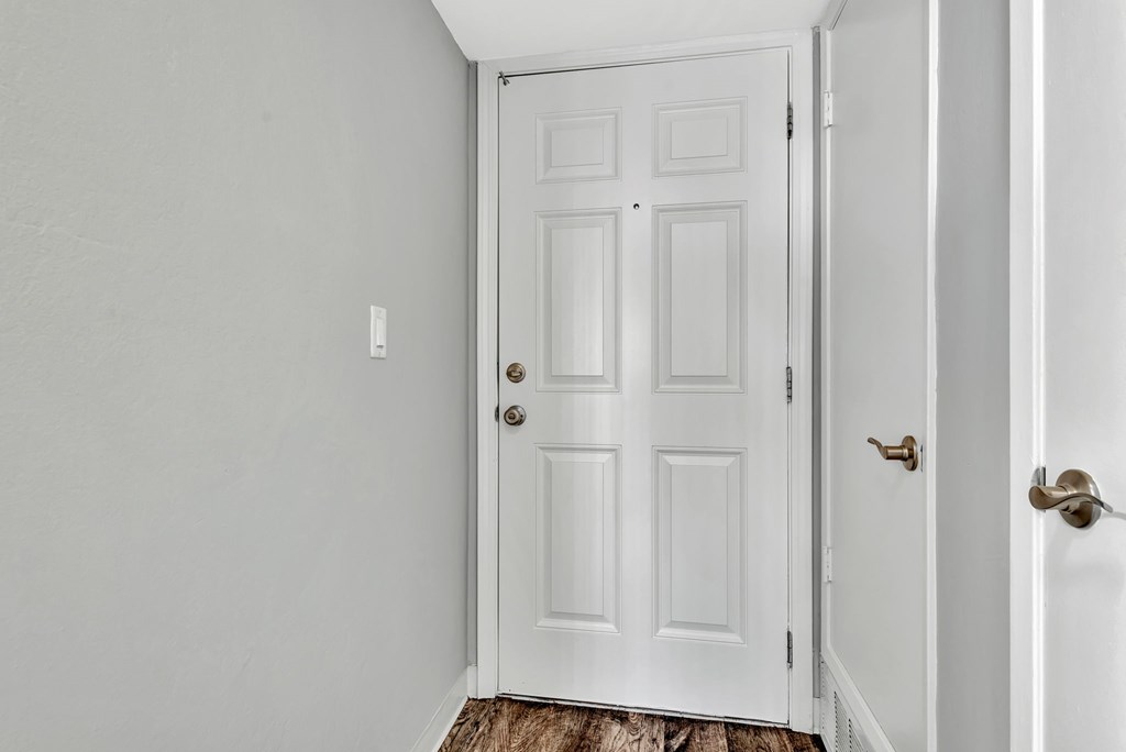 A white door with a brass handle is in a white room.