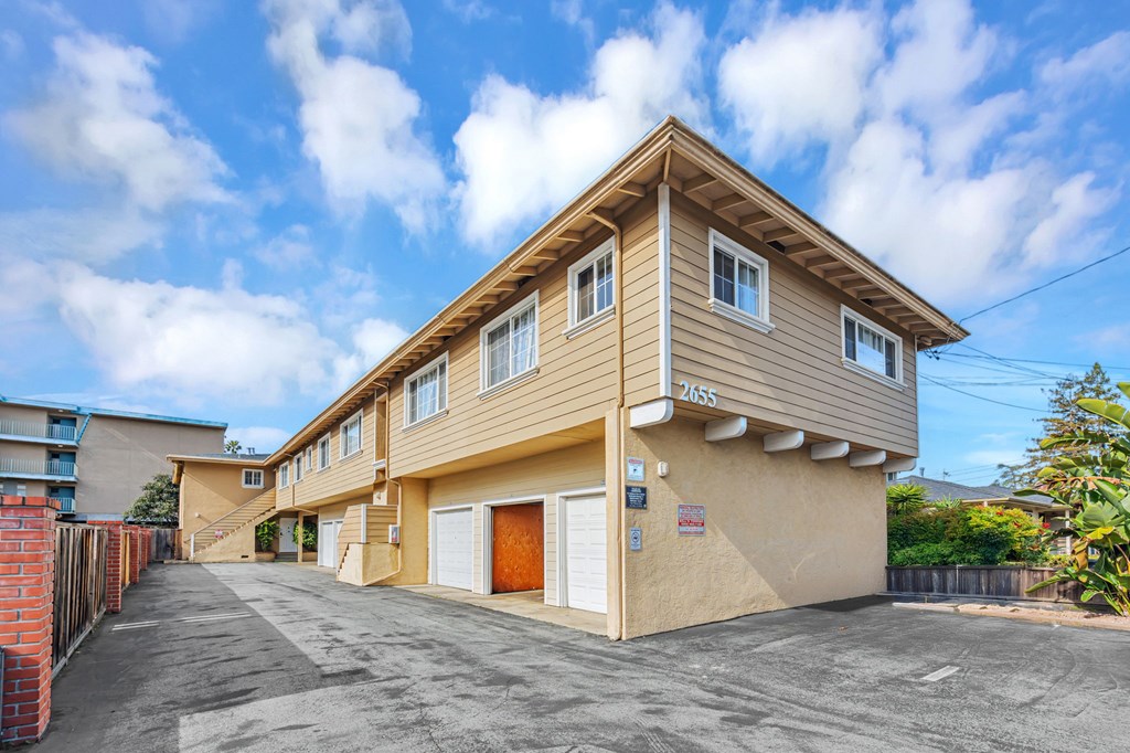 A two-story residential building with a garage is surrounded by a fence and has a clear blue sky above.