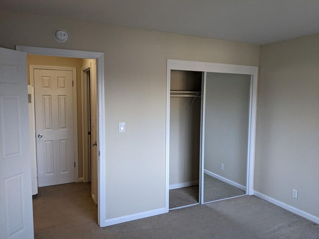 A room with a white door and a white closet with a mirror.