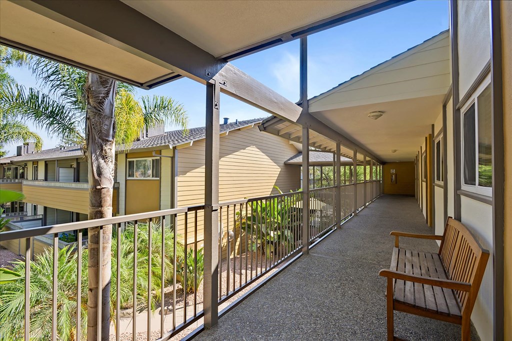 a long balcony with a wood bench and a building in the background