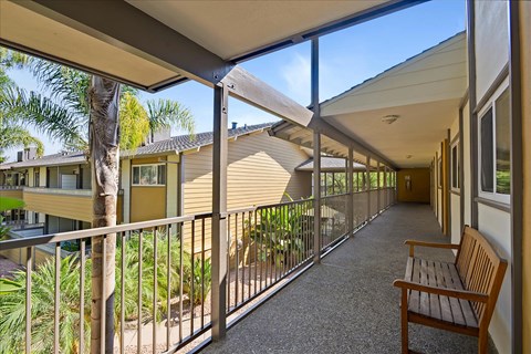 A wooden bench sits on a patio with a metal railing.