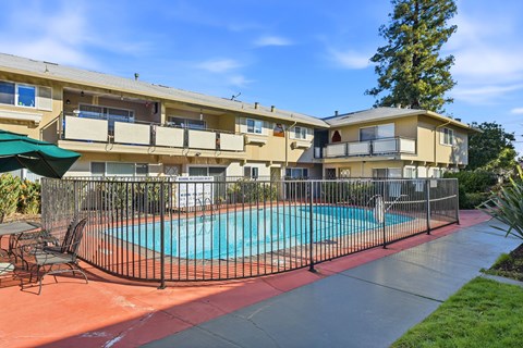 A pool surrounded by a black fence and chairs.