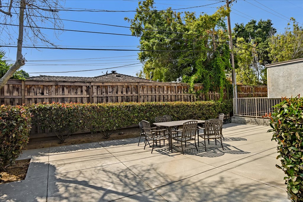 A patio with a table and chairs is surrounded by a hedge and a wooden fence.
