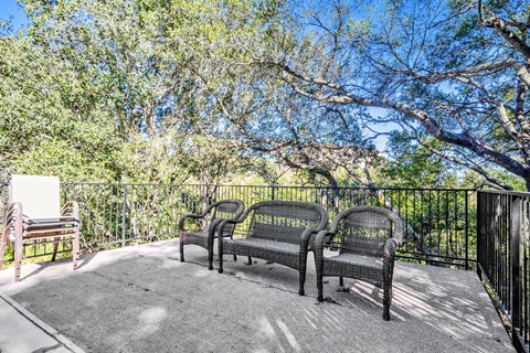 A patio with three wicker chairs and a table.