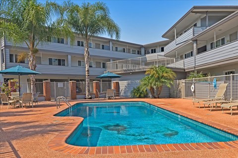 A swimming pool surrounded by a patio with chairs and umbrellas.