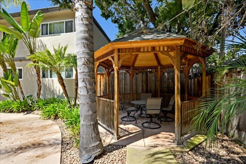 A wooden gazebo is surrounded by trees and plants.