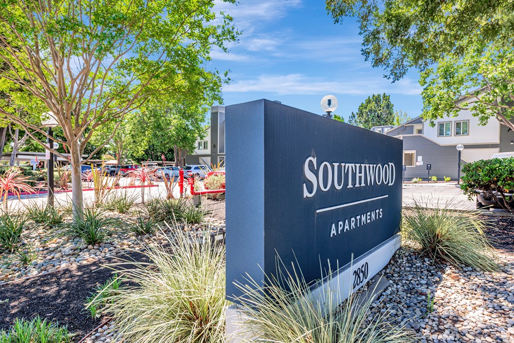 A sign for Southwood Apartments is in front of a tree and some bushes.