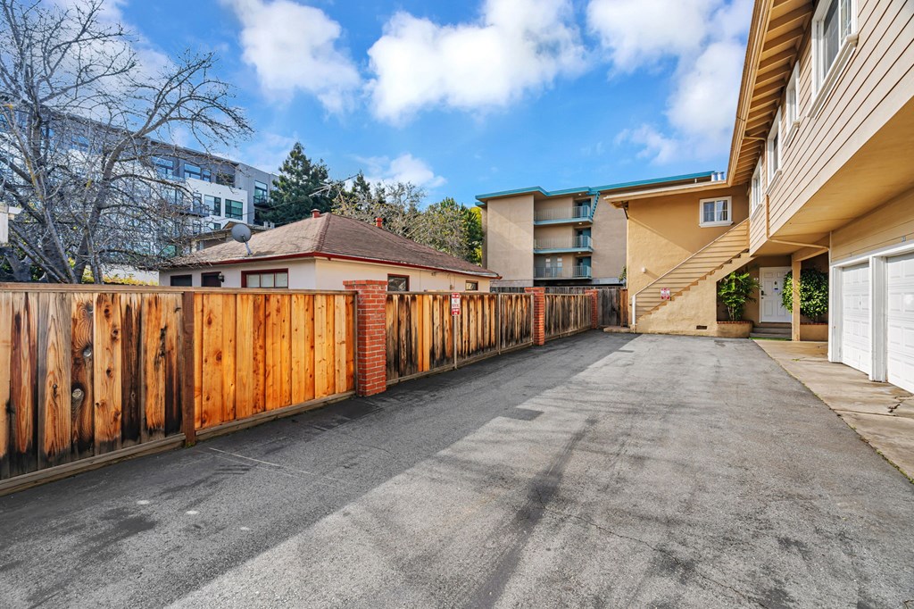 A long driveway with a wooden fence on the left side and a building on the right.
