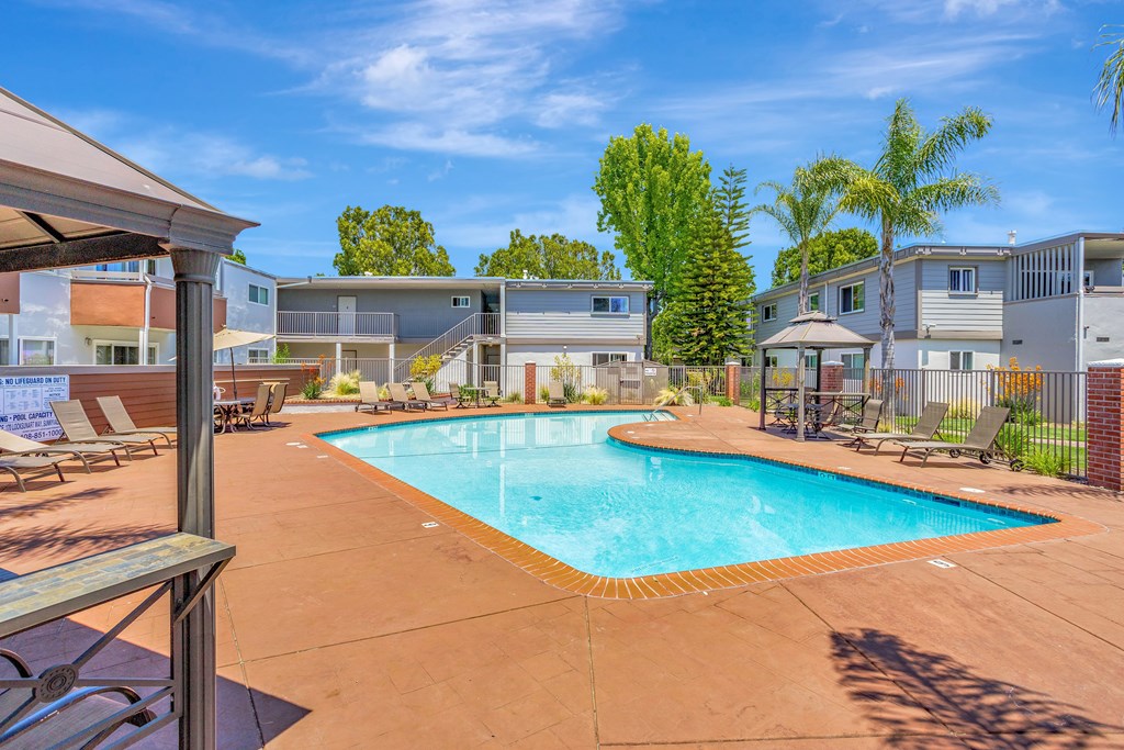 A swimming pool surrounded by a patio with chairs and a building in the background.