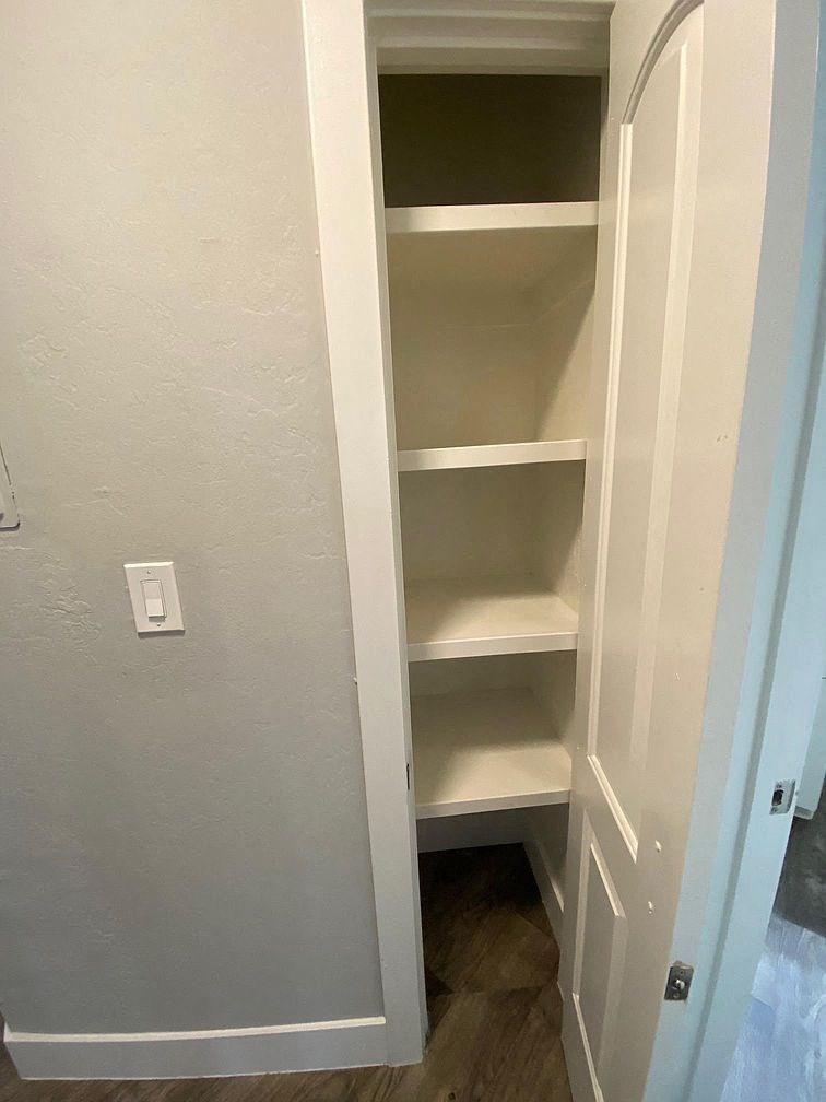 A white closet with shelves and a light switch on the wall.