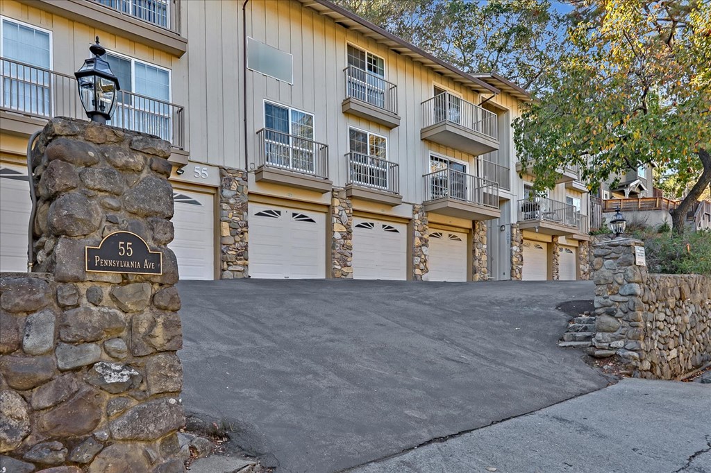 a driveway with a stone wall in front of a building with white garage doors