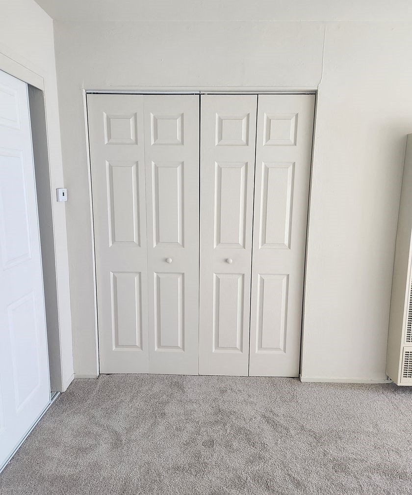 A room with a white door and a grey carpet.