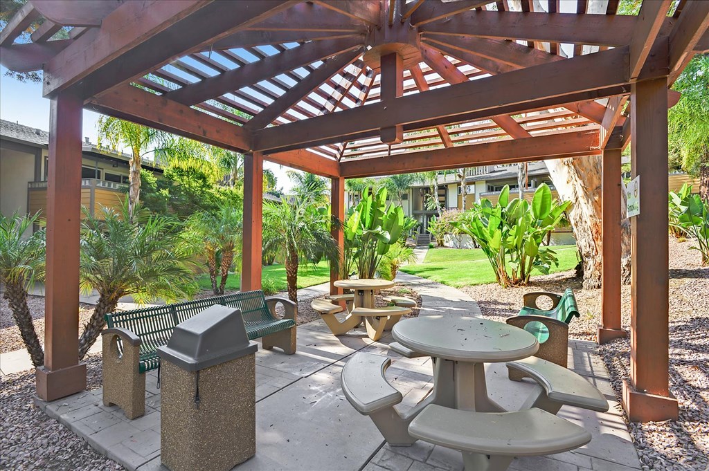 a patio with tables and benches under a wooden pavilion