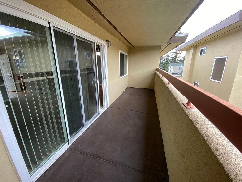 A balcony with glass doors and a brown floor.