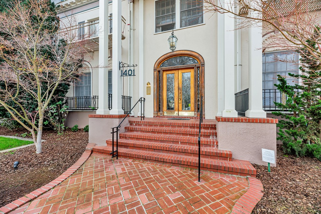 A white house with a brown door and a brick pathway leading to it.