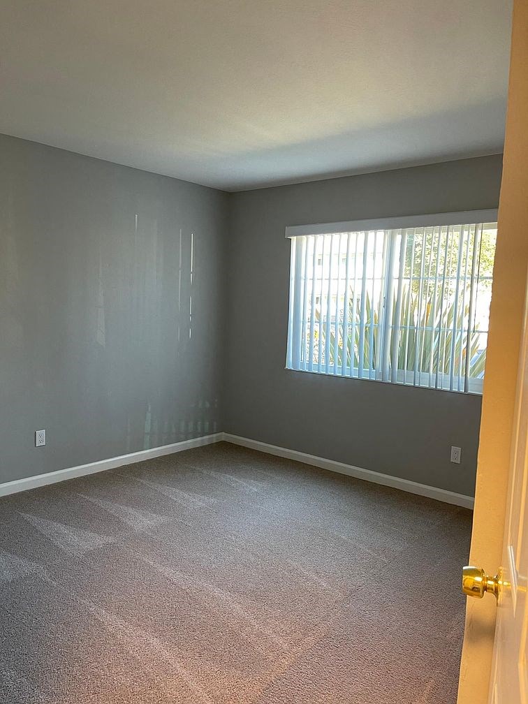 A room with a carpeted floor and a window with blinds.