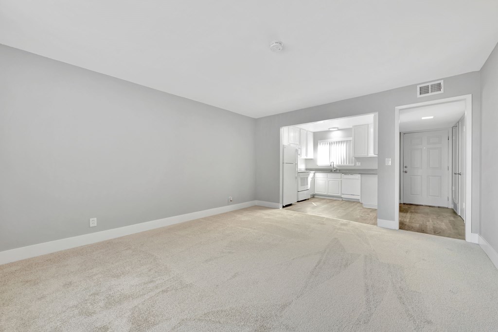 A large, empty room with a carpeted floor and a doorway leading to another room.
