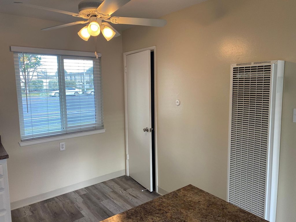 A room with a ceiling fan, a window with blinds, a door, and a wall-mounted air conditioning unit.