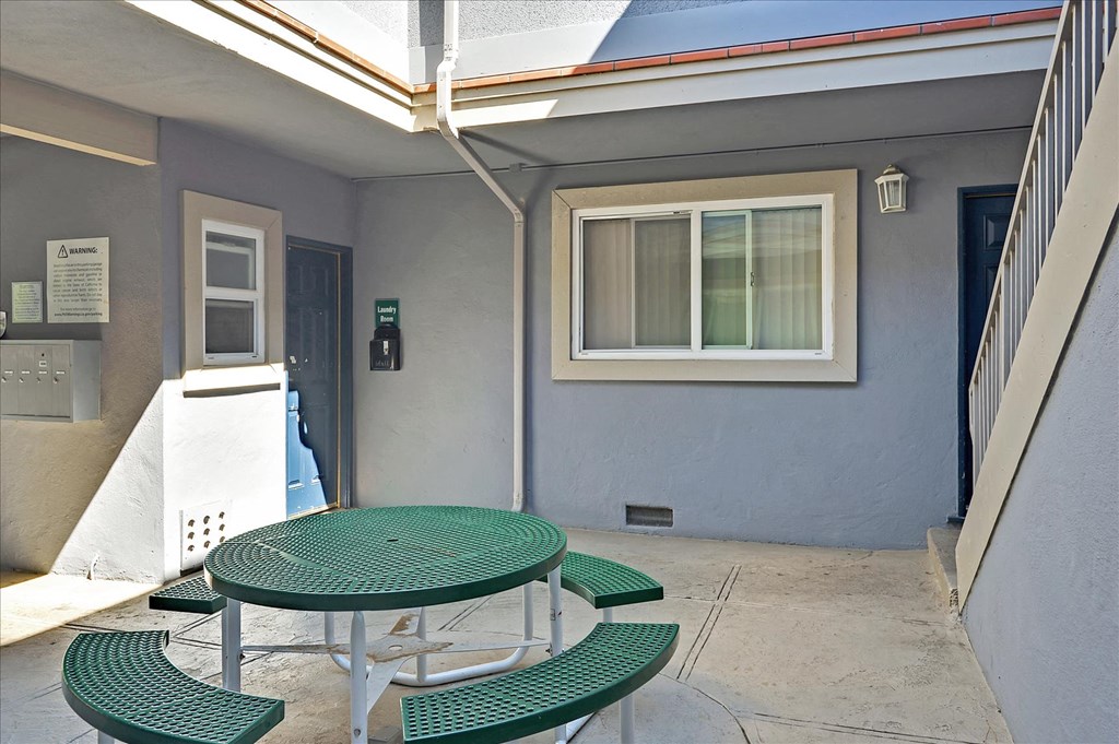 A green table and benches are set up outside a building.