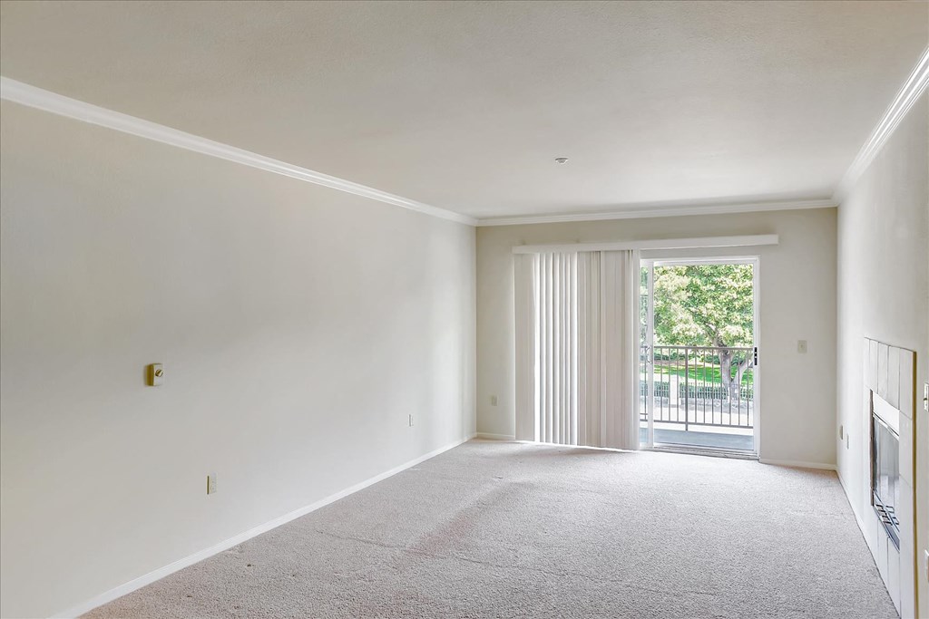 A large, empty room with a carpeted floor and a sliding glass door leading to a balcony.