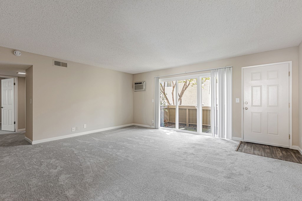 A spacious room with a carpeted floor and a window with blinds.