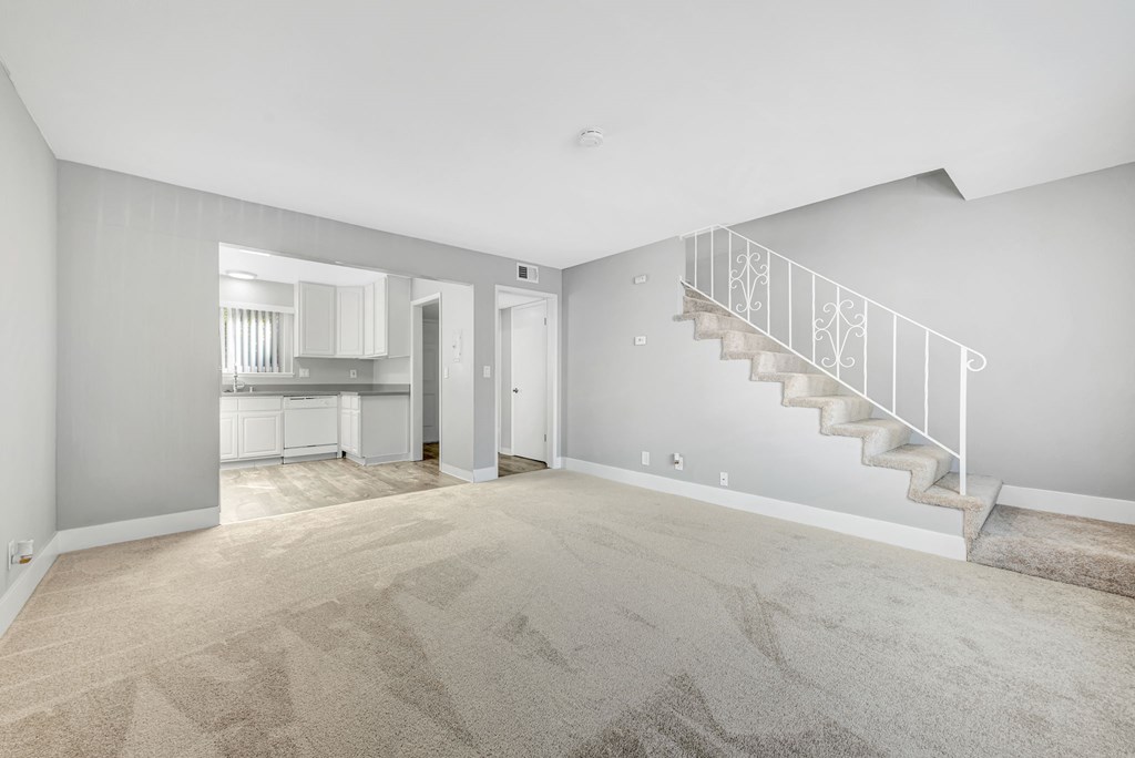 A spacious room with a staircase and a kitchen in the background.
